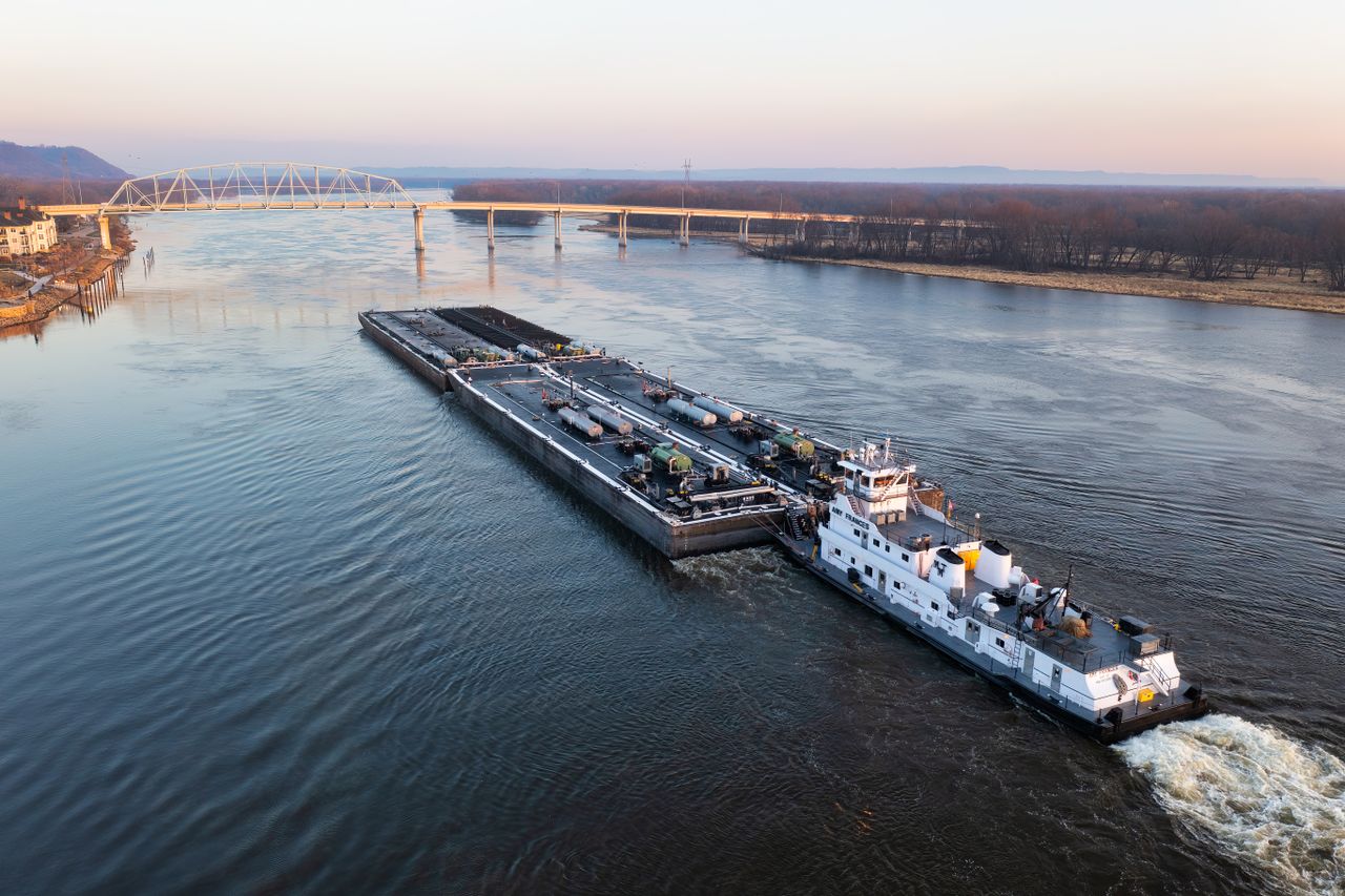 A large barge navigates the Mississippi River near a bridge in Wabasha, Minnesota.