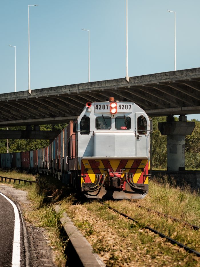 services-07 Freight train passing under a bridge in Laguna, Brazil, during daylight.